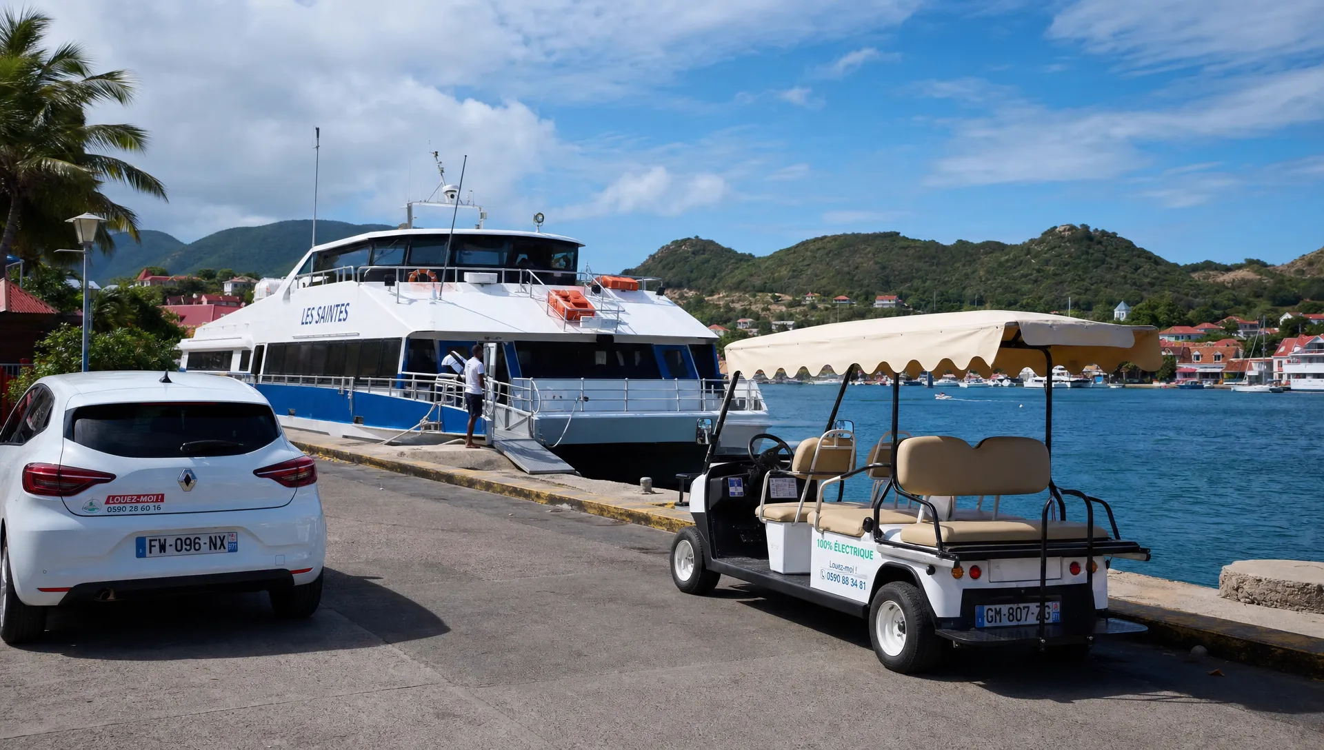 Un bateau-navette au port avec une voiture de location stationn&eacute;e c&ocirc;t&eacute; quai en Guadeloupe, et une voiturette &eacute;lectrique 4 places attendue sur le d&eacute;barcad&egrave;re de Terre-de-Haut.