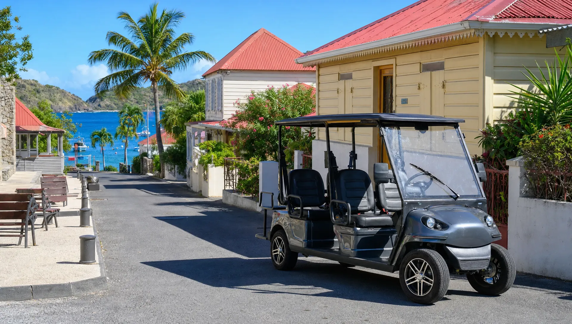 Une voiturette électrique quatre places stationnée dans le bourg de Terre-de-Haut, avec des maisons créoles, des palmiers et la mer au loin.