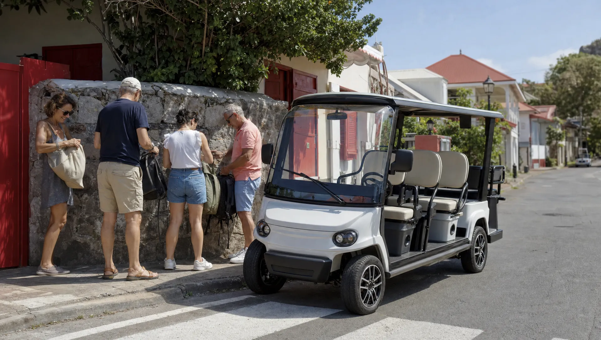 Une voiturette électrique 4 places attend au bord d’une rue calme de Terre-de-Haut pendant que quatre adultes préparent leurs sacs légers.
