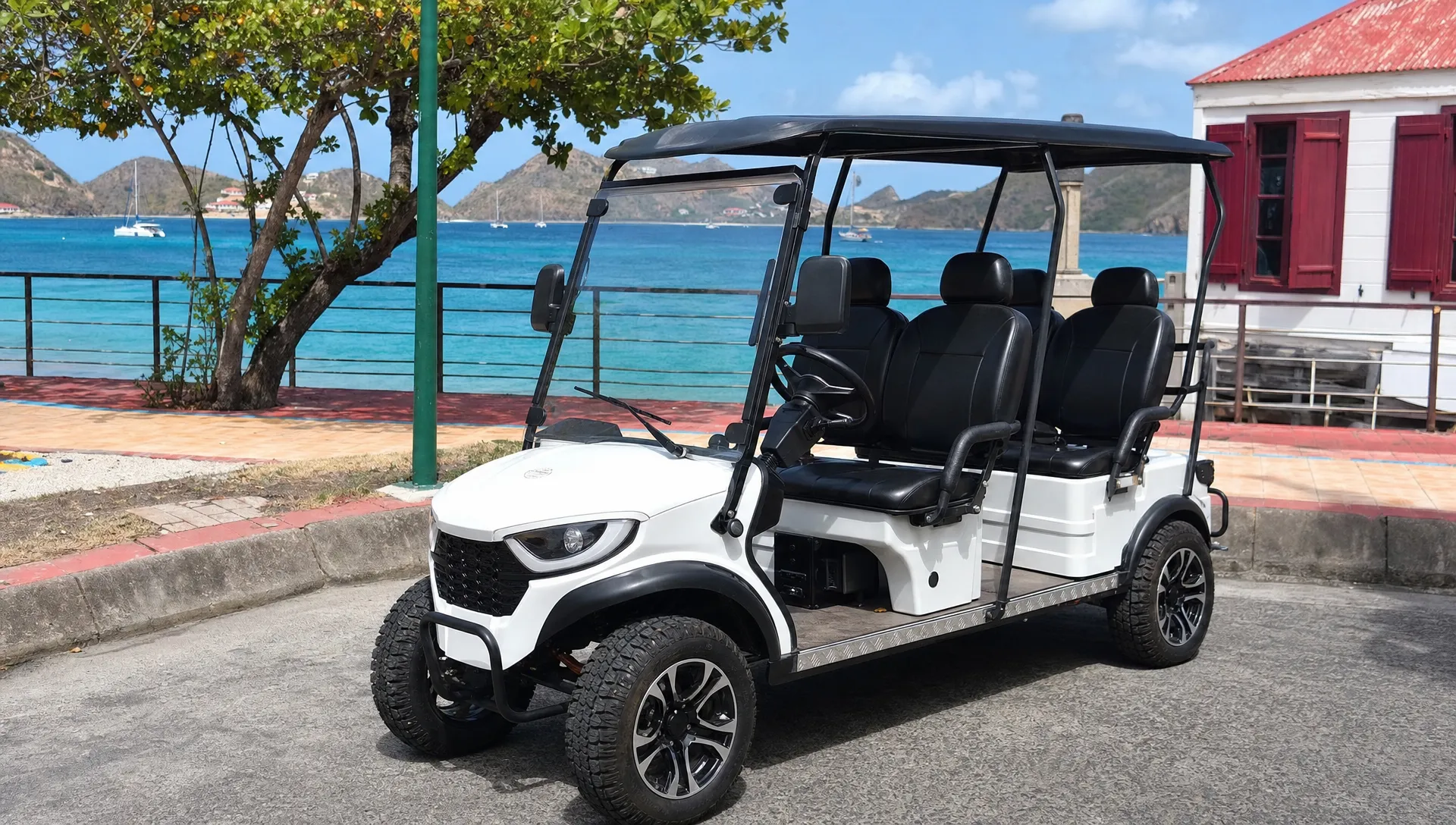 Une voiturette électrique 4 places est stationnée dans une rue de Terre-de-Haut, avec la mer des Saintes en arrière-plan.